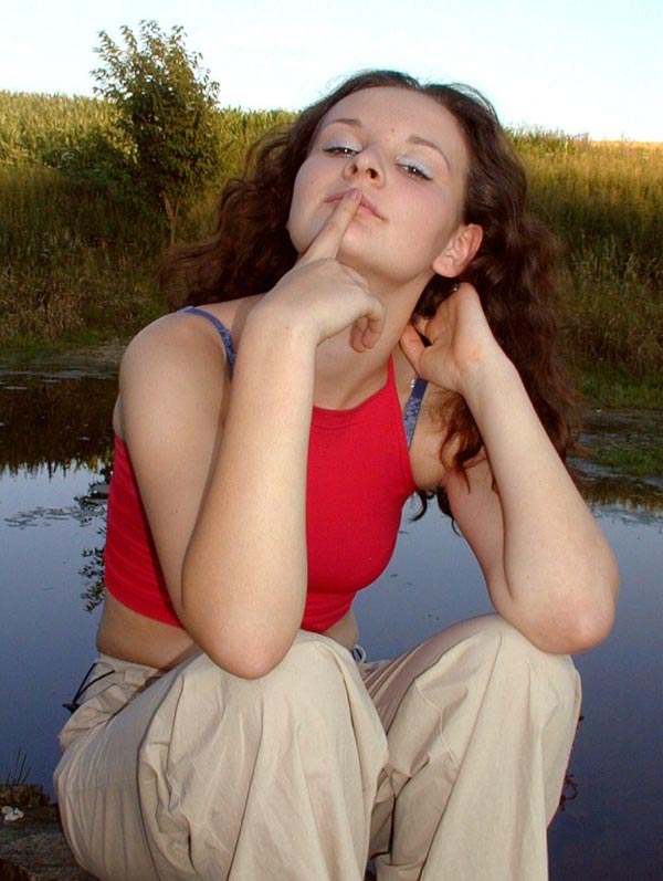 junge Brünette mit rotem Oberteil sitzt am Teich